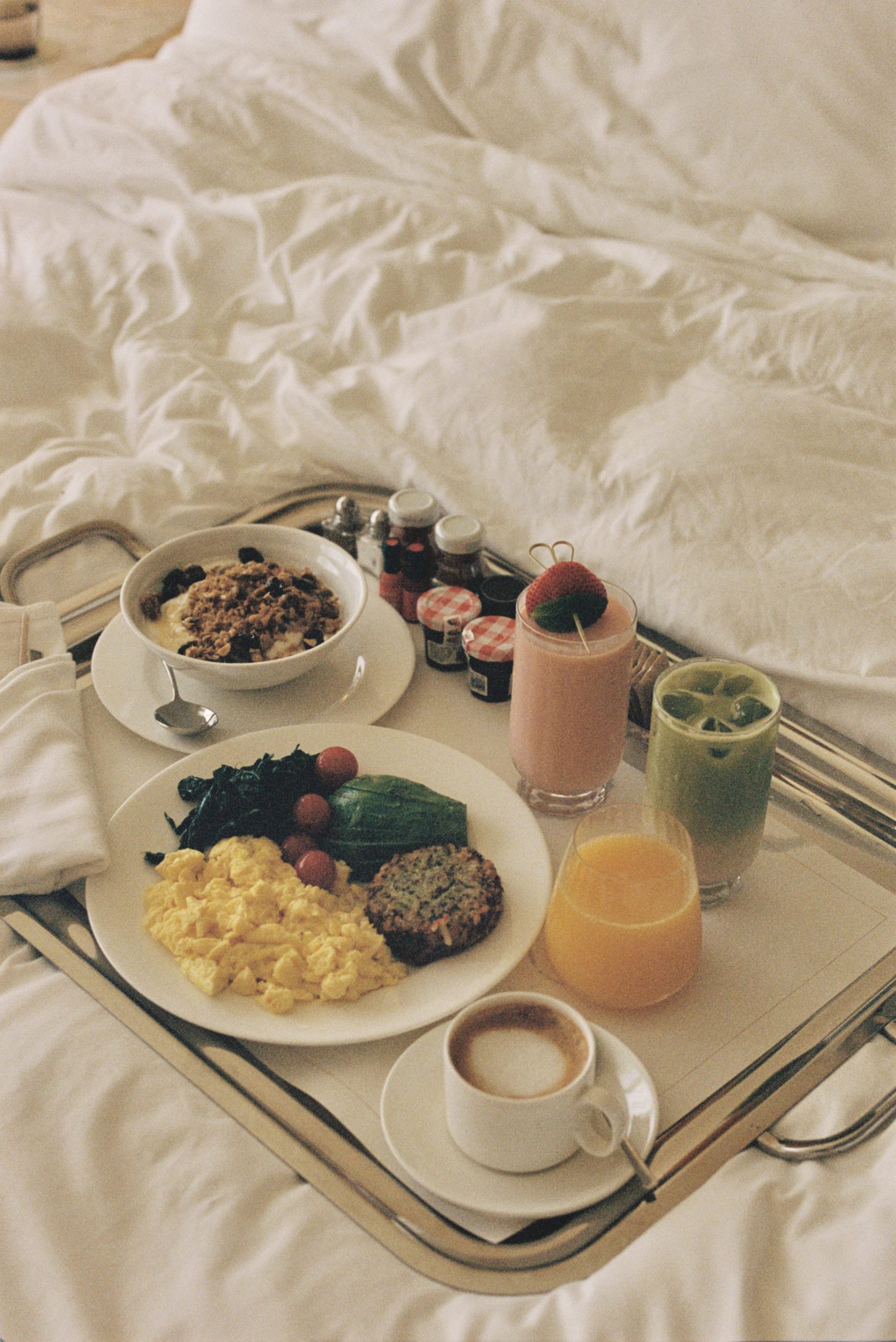 Luxury in room breakfast tray with eggs, granola, fresh juices, coffee, and smoothies served on a cozy hotel bed with white linens