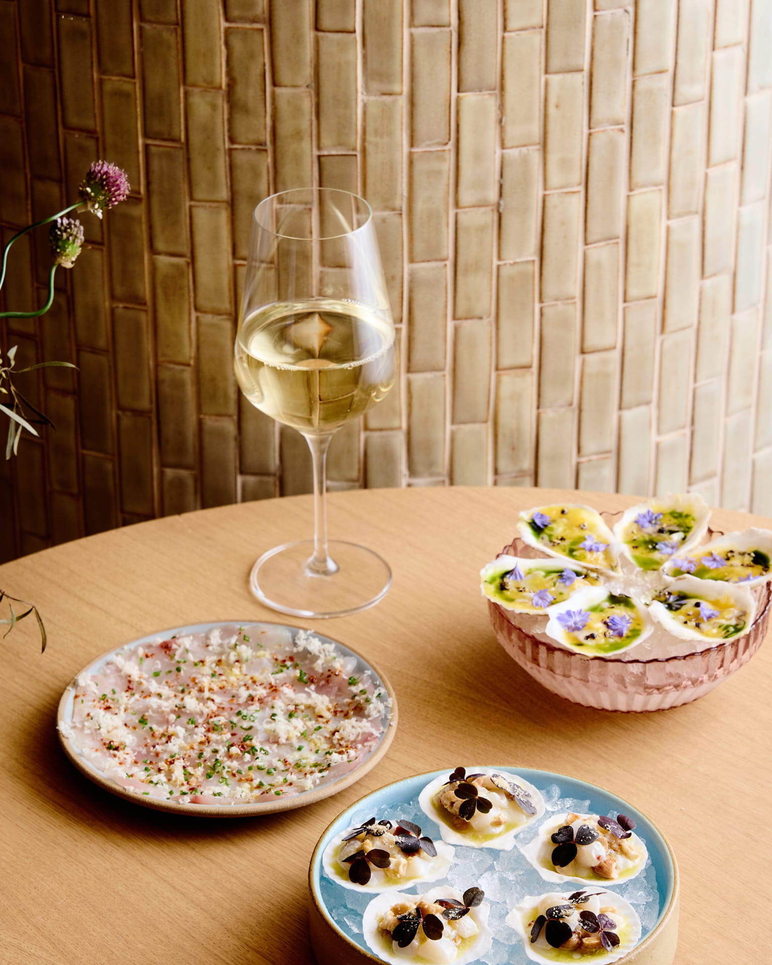 Elegant seafood and oyster spread with white wine served on a wooden table against a warm textured tile backdrop